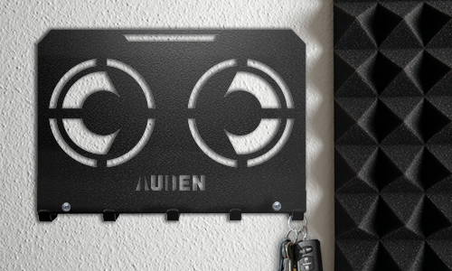 Portachiavi da parete in metallo con design geometrico intagliato e nome personalizzato, montato su una parete strutturata